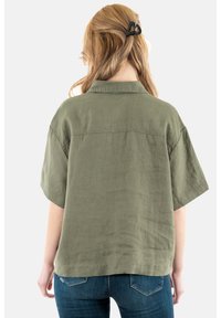 Camicia verde oliva a maniche corte con colletto, realizzata in tessuto leggero, caratterizzata da una vestibilità comoda e semplici dettagli di cucitura.