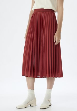 Gonna midi plissettata rossa con vita alta, realizzata in tessuto leggero. Abbinata a calze bianche e scarpe con tacco a blocco color avorio.