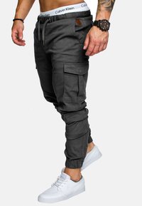 Graue Cargo-Jogginghosen aus strapazierfähigem Stoff mit elastischem Bund, zulaufenden Beinen und mehreren Taschen. Kombiniert mit weißen Turnschuhen.