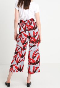 Vida byxorna i ljusgrått tyg med ett djärvt rött och svart bladmönster. Elastisk midja och ledig passform. Matchas med en vit topp.