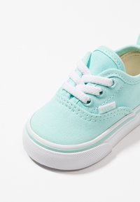 Vaalean teal väriin kuuluva kangaskenkä, jossa on valkoiset nauhat ja kumipohja. Sivussa on pieni logotagi ja pintamateriaali, joka tarjoaa hyvän pidon.