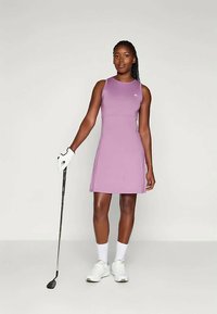 Kortärmad golfklänning i ljuslila, designad med en figurnära silhuett och mjuk tyg, med logotypdetalj och sidofickor.