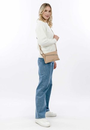 Borsa crossbody color nocciola con finitura testurizzata e zip argentata, abbinata a un maglione crema e jeans azzurri chiari, su uno sfondo bianco.