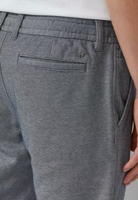 Grijze, gestructureerde stoffen broek met een achterzak met een horizontale opening en een klein metalen merkembleem op de tailleband.