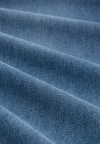 Close-up van opgevouwen blauwe denimstof die de textuur en het diagonale weefpatroon laat zien.