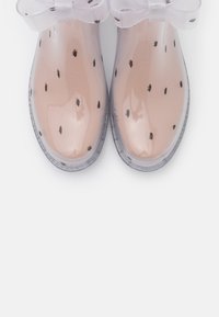 Transparent pink jelly shoes with black polka dots, rounded toe, and soft, sheer ribbon bow on the ankle. Smooth, glossy texture.