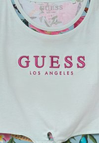 Biały krótki top bawełniany z różowym haftowanym logo "GUESS LOS ANGELES", okrągłym dekoltem i ozdobnym kwiatowym wzorem na podszewce wewnętrznej.
