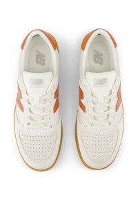Zapatillas blancas con acentos naranjas, puntera perforada y suela texturizada en tono marrón. Presentan cordones y logotipo en la lengüeta. Diseño clásico.