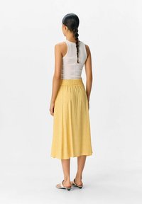 Jupe midi jaune à pois avec taille élastique, associée à un débardeur blanc ajusté. Tissu lisse et silhouette décontractée.