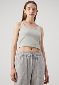 Débardeur gris court avec de larges bretelles et un décolleté carré, associé à un pantalon à rayures gris clair avec cordon de serrage, fabriqué en tissu doux.