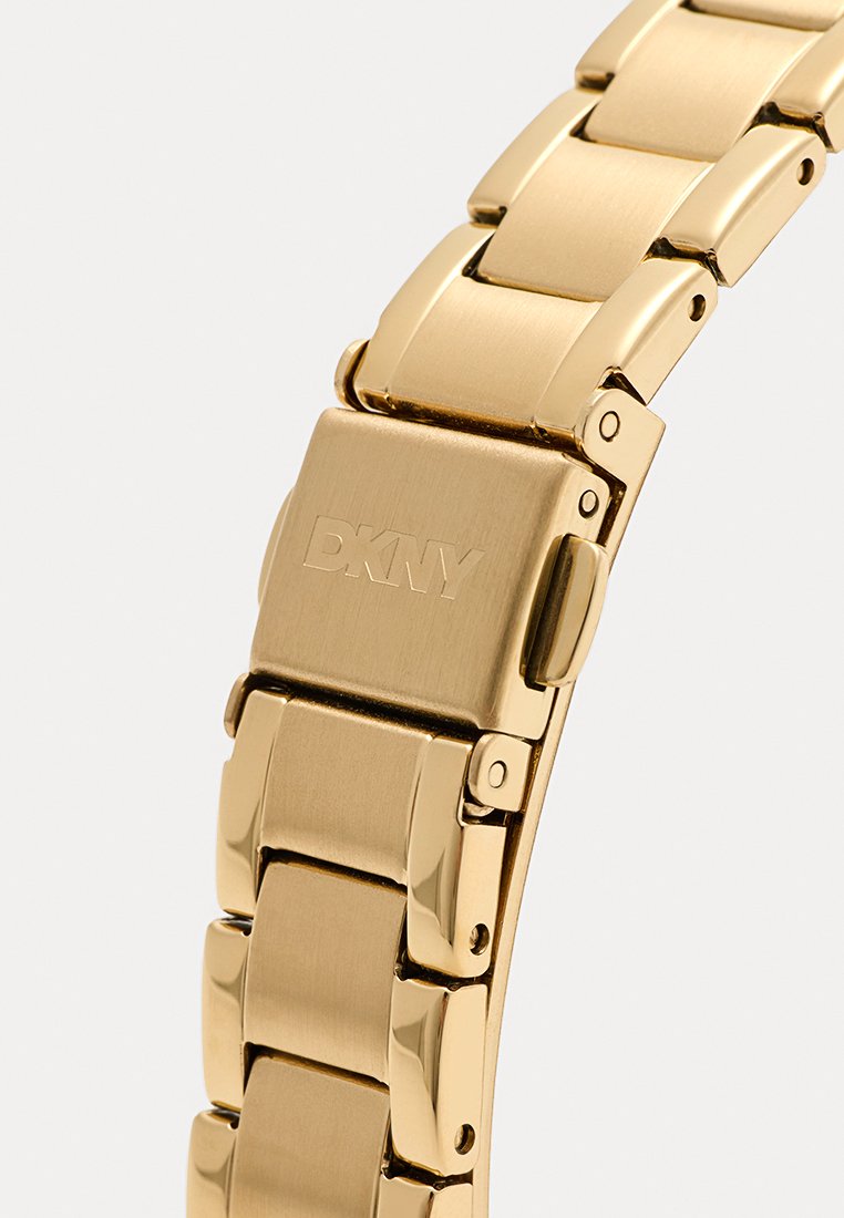 Gouden roestvrijstalen horlogeband met platte, gestructureerde schakels, een gegraveerde sluiting van DKNY en een gladde afwerking voor een strakke uitstraling.