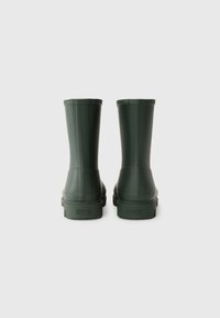 Bottes de pluie en caoutchouc vert avec une finition lisse, d'une hauteur mi-mollet, au design strié et aux semelles texturées, arborant le nom de la marque à l'arrière.