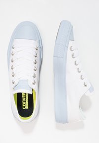 Baskets en toile blanche avec une semelle et un bout en caoutchouc bleu clair, dotées d'œillets argentés, de lacets blancs et d'une semelle intérieure jaune vif.