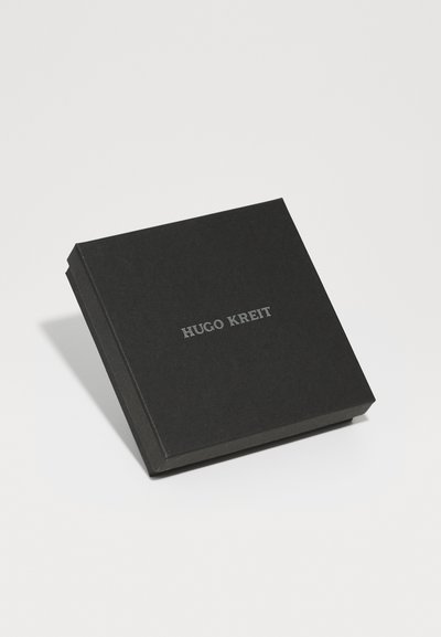 Caja cuadrada negra con un acabado mate, que presenta el nombre grabado "HUGO KREIT" en letras plateadas en la parte frontal.
