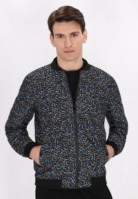 Giacca bomber nera con un motivo di foglie colorate, polsini e colletto a costine e chiusura frontale con zip. Il tessuto testurizzato aggiunge profondità.