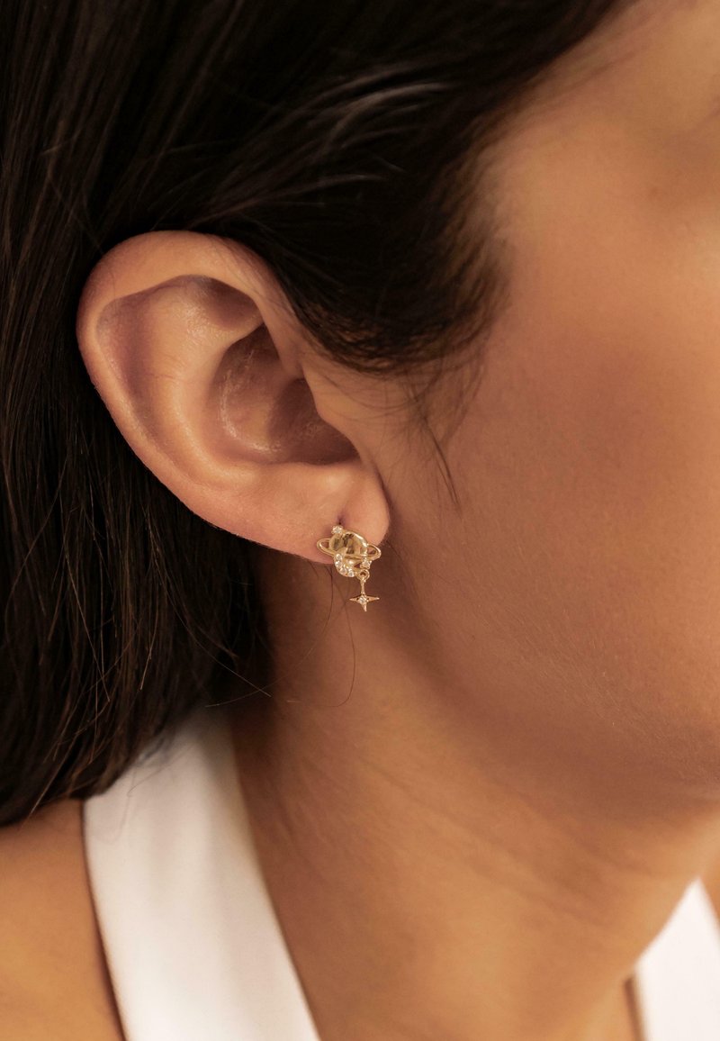 Goldohrringe mit einem Planeten-Design und einem kleinen funkelnden Akzentanhänger. Sie werden am Ohrläppchen getragen und zeigen eine zarte, filigrane Form.