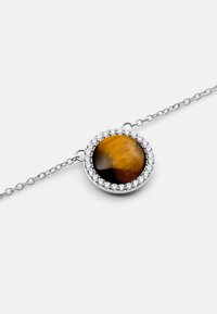Bracciale in argento con una pietra tonda di occhio di tigre circondata da un cerchio di piccole cristalli trasparenti. Superficie liscia, finitura lucida.