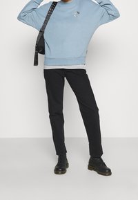 Felpa azzurro chiaro con scollatura rotonda e dettagli ricamati, abbinata a pantaloni neri slim-fit e stivali neri stringati.