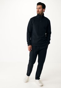 Conjunto deportivo en azul marino que incluye un sudadera con cuello zip y pantalones a juego, ambos de corte relajado, con zapatillas blancas.