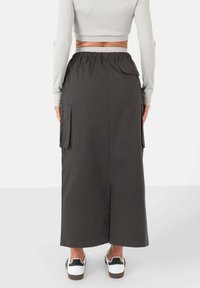 Lange donkergrijze rok van een katoenmix, met zijzakken en een split aan de achterkant, gedragen met witte sneakers en een grijze crop top.