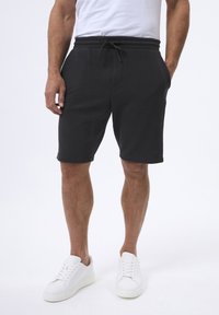 Sorte teksturerede shorts med elastisk talje og snøre, der har sidelommer, parret med hvide sneakers.