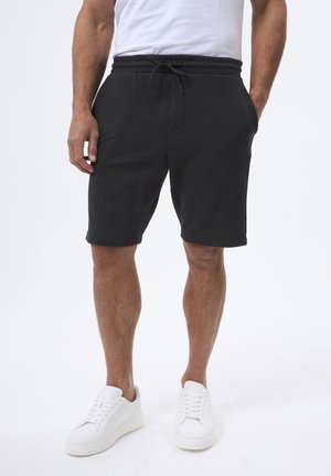 Schwarze, strukturierte Shorts mit elastischem Bund und Kordelzug, ausgestattet mit Seitentaschen, kombiniert mit weißen Sneakern.