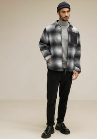 Grå och svart rutig jacka med en svart bröstficka, grå polotröja, svarta byxor och kraftiga svarta stövlar. Slät textur, avslappnad passform.