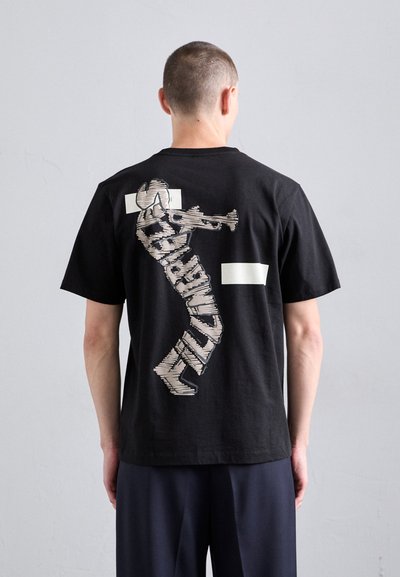 T-shirt en coton noir avec un grand design graphique au dos, affichant un texte stylisé et une figure dans des tons crème.