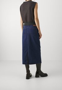 Tumma neuleilma sleeveless toppi, jossa on ribattu pinta, yhdistettynä pitkään tummansinsiseen farkkuhameeseen, jossa on kaksi takataskua ja keskilahje. Mustat saappaat.