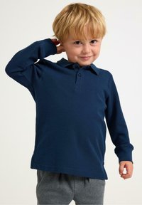 Navy long-sleeve polo shirt with a collared neck and button placket, made from textured cotton fabric. Paired with gray patterned pants.