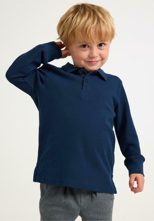 Navy long-sleeve polo shirt with a collared neck and button placket, made from textured cotton fabric. Paired with gray patterned pants.