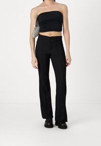 Zwarte strapless top met gegatherde textuur, gecombineerd met hoge zwarte flared broeken met verticale naden en zakken. Zwarte schoenen en een zilveren tas.