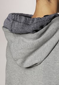 Szary hoodie z teksturowanym, czarno-białym wzorem wewnętrznego podszycia kaptura. Miękki materiał, o luźnym kroju i lekkim rozciągnięciu.