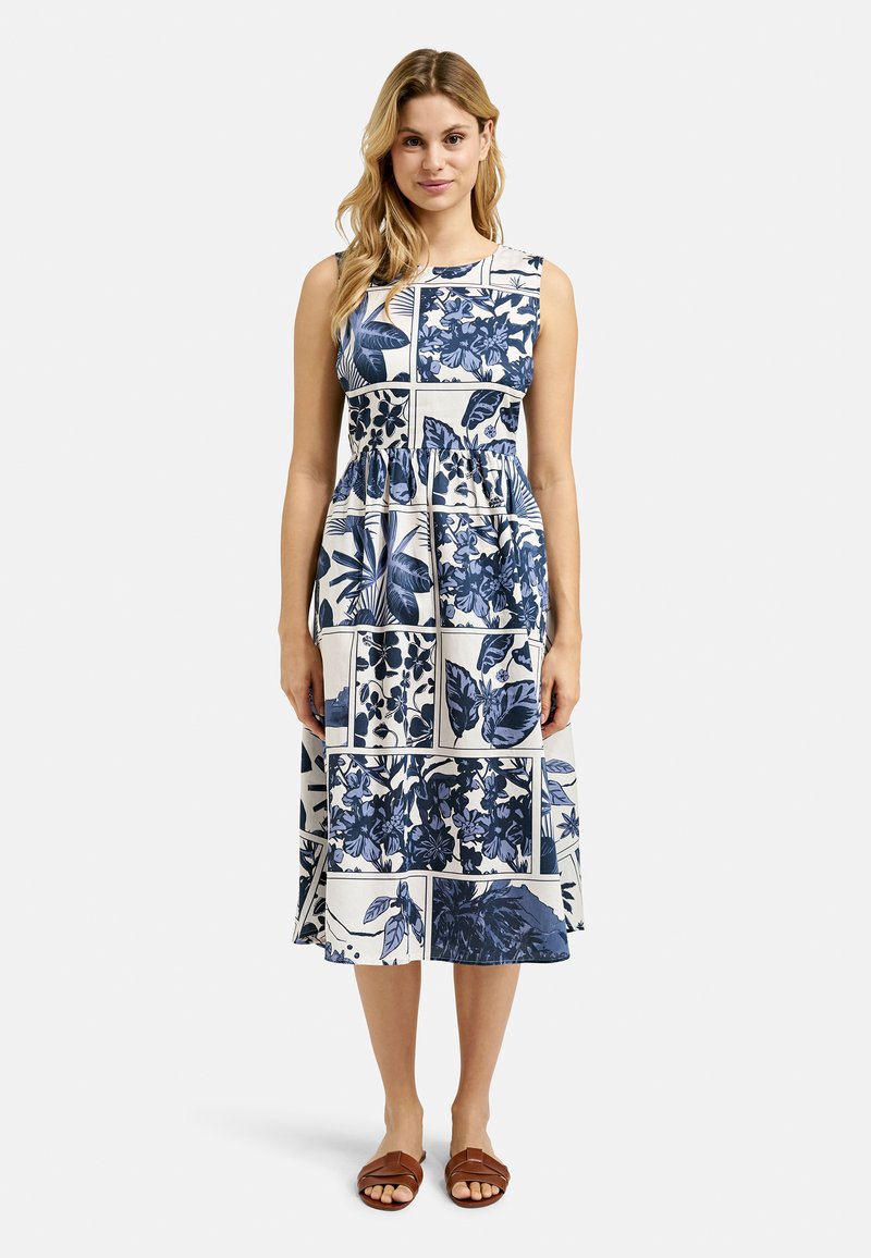 Blumenmusterkleid in Marineblau und Weiß, mit tailliertem Oberteil, gerafftem Taillenbereich und A-Linie-Rock; getragen mit braunen Sandalen.