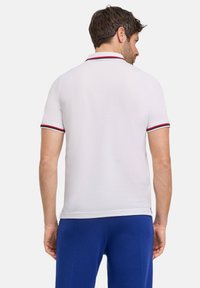 Biała koszulka polo z krótkim rękawem. Posiada czerwono-granatowe paski na kołnierzyku i rękawach. Gładka tekstura, dopasowany krój.