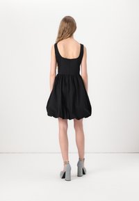 Μαύρο αμάνικο φόρεμα με στρογγυλή πλάτη, gathered φούστα και υφή υφάσματος. Φορεμένο με γκρι παπούτσια με τετράγωνο τακούνι.