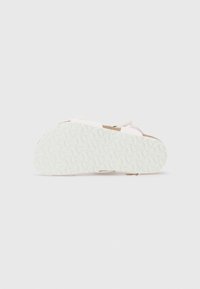 Vitt sandalsole med ett texturerat mönster med spår, kontrasterande bruna accenter nära hälen och ljusa remmar.