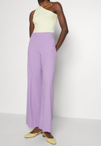 Geel geribbeld top met één schouder, gecombineerd met wijde lavendelkleurige broeken en gele lage hakken. Zachte texturen, ontspannen pasvorm.