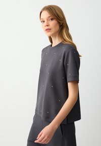 Grijze sweatshirt met korte mouwen en een ontspannen pasvorm, met verspreide rhinestones op de voorkant en een ronde halslijn.