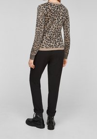 Pull beige avec imprimé léopard noir, poignets et ourlet côtelés. Associé à un pantalon noir et des bottes noires à lacets.