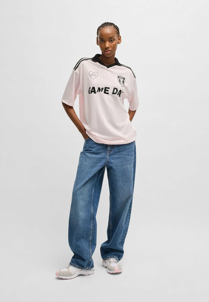 Pink short-sleeve polo shirt with black collar and "GAME DAY" text. Paired with loose-fitting, blue denim trousers and athletic shoes.