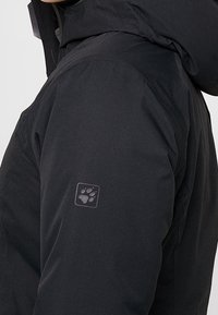 Svart isolerad jacka med huva, slät textur och en subtil tassavtryck-logotyp på vänster ärm. Vattentätt material.