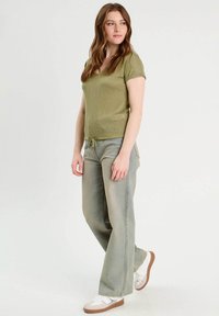 Haut texturé vert olive avec un col en V et des manches courtes, associé à un jean large bleu clair avec taille à cordon et des baskets blanches.