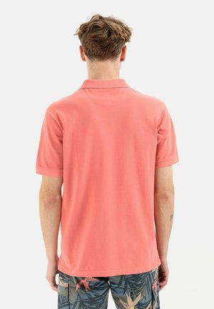 Polo corail à manches courtes et col classique, fabriqué en coton doux. Le dos présente une texture lisse sans embellissements.