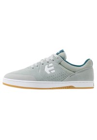 Světle šedé semišové skate boty s bílým logem, perforovanou stranou a akcenty v teal barvě. Bílá gumová podrážka s hnědou gumovou vnějším podrážkou.