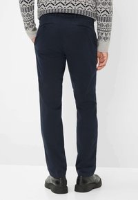 Pantaloni in cotone blu navy con tasche posteriori e vita aderente, abbinati a scarpe nere e a un maglione grigio a fantasia.