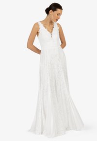 Robe longue en dentelle blanche avec un décolleté en V, des motifs floraux élaborés et une jupe fluide. Elle possède une taille cintrée et des bretelles délicates.