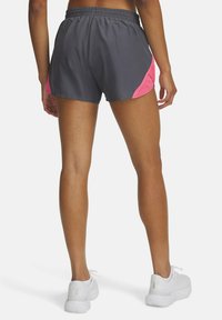Grå idrottsshorts med rosa nätdetaljer på sidorna, elastisk midja och avslappnad passform, tillsammans med vita sneakers på bara ben.