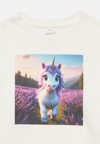 Λευκό βαμβακερό t-shirt με έντονα χρώματα και εκτυπωμένο μονόκερο με μωβ χαίτη, σε φόντο λιβάδι λεβάντας και βουνά στο παρασκήνιο.