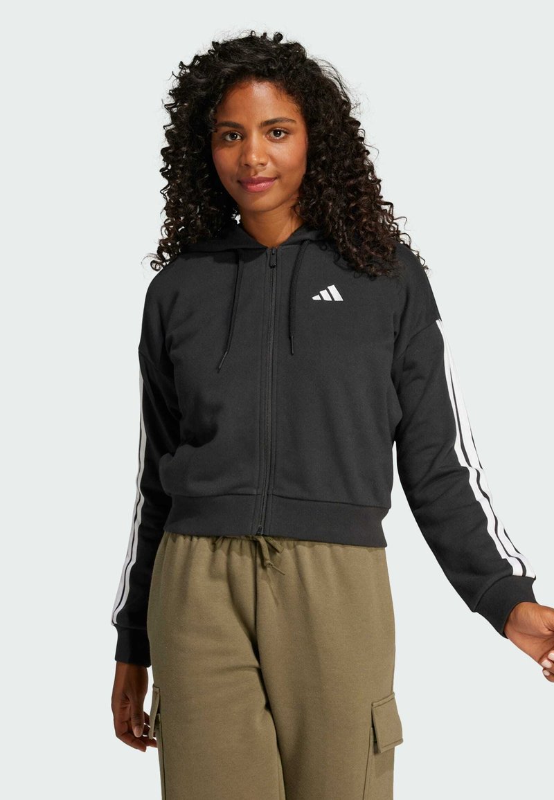 Must have tõmblukuga must kapuutsiga sviiter, millel on string ja valge Adidas logo rinnas; harjad on valgetes triipudes varrukatel.